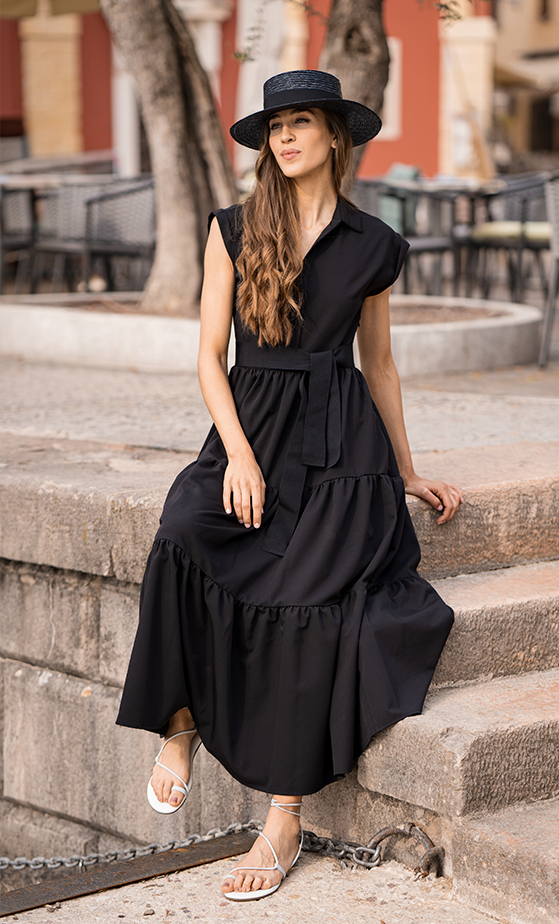 Frau auf einer Mauer im schwarzen Sommerkleid